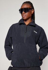 Marineblauwe fleece pullover met een kwart-rits aan de voorkant en een zwart paneel, voorzien van een elastische zoom en zakken, met een Columbia-logo op de borst.