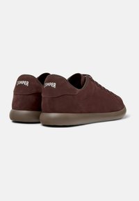 Burgundy suede sneakers with a round toe, low-top design, rubber sole, and white "CAMper" logo on the heel. Minimalist and sleek appearance.