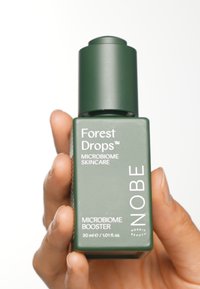 Grön rektangulär flaska med en cylindrisk kork. Etiketten visar "Forest Drops Microbiome Skincare" i vit text. Innehåller 30 ml av produkten.