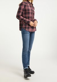 Röd och svart rutmönstrad skjorta med knappar och långa ärmar, matchad med blå jeans och svarta snörkängor. Skjortan har en rundad nederkant.