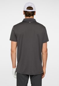 Mörkgrå polo skjorta med klassisk krage, korta ärmar och en slät yta. Har en logotyp på baksidan nära halsringningen.