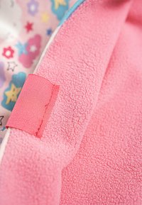 Tela de forro rosa con textura suave, que presenta una etiqueta de satén rosa en contraste. El fondo incluye una tela colorida y estampada con estrellas y flores.