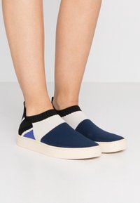 Stickade slip-on skor med en färgblockdesign i blått, krämfärg och svart med en strukturerad yta. Gummisulor och ankellängd.