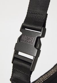 Black nylon strap featuring a sturdy black plastic buckle with the engraved brand name "DIESEL." Fine texture with reinforced stitching.