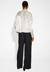 Camicia di satin beige chiaro con un taglio morbido, colletto a revers, maniche lunghe e piega sul retro, abbinata a pantaloni neri a gamba larga.