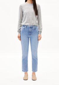 Ljusgrå långärmad skjorta, högmidjade ljusblå jeans med raka ben och beige slip-on skor mot en enfärgad bakgrund.