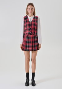Vestito mini a quadri con parte superiore a giacca aderente in motivo check nero e rosso, gonna plissettata, abbinato a stivaletti neri alla caviglia.