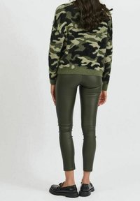 Grön kamouflage-mönstrad fluffig tröja med långa ärmar, ihopparad med högmidjade olivgröna imitationläderleggings och svarta slip-on skor.