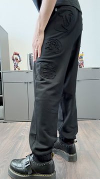 Schwarze Hose mit lockerer Passform, ausgestattet mit gestickten Logodetails an den Taschen. Kombiniert mit schwarzen Plateauschuhen und einer strukturierten Sohle.