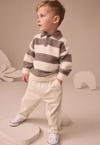 Pull à rayures multiples en crème et gris avec un col, associé à un pantalon côtelé crème et des baskets blanches. Textures simples et douces.