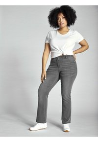 Jeans de mezclilla gris acampanados con una cintura alta, con cinco bolsillos y un ligero desvanecimiento. Combinados con una camiseta blanca atada y zapatillas blancas.