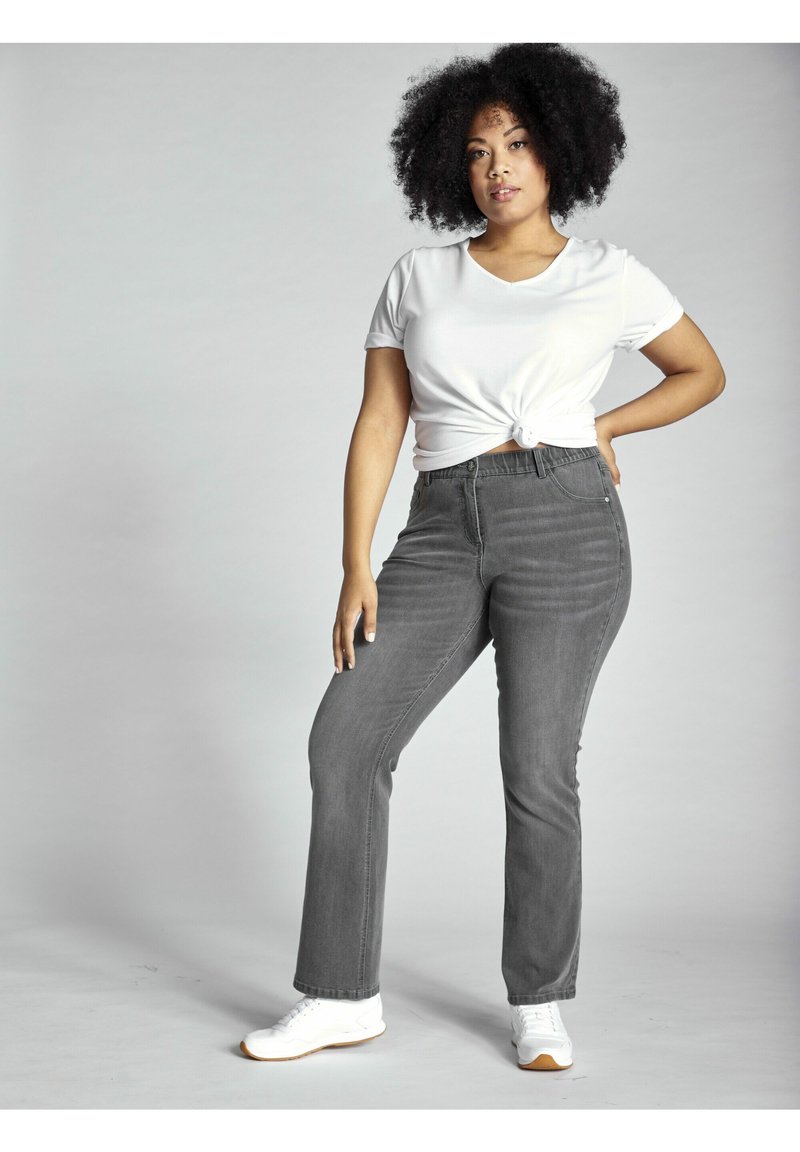 Jeans de mezclilla gris acampanados con una cintura alta, con cinco bolsillos y un ligero desvanecimiento. Combinados con una camiseta blanca atada y zapatillas blancas.