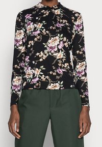 Maglietta nera a maniche lunghe con un motivo floreale in viola, bianco e verde. Design a collo alto con dettagli arricciati al colletto.