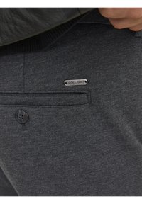 Mörkgrå byxor med en strukturerad tyg, med en klassisk knappstängning och en metallskylt märkt "JACK & JONES" på fickan.