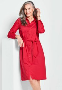Rode knoopjurk met lange mouwen, een ceintuur in de taille en een split aan de voorkant. Gemaakt van een soepele, textuurstof.