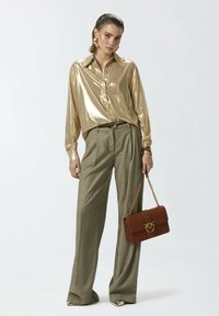 Metalna zlatna košulja na dugmad, hlače s visokim strukom u karirano, smeđa torba s zlatnim detaljima i cipele s oštrim vrhom s metalnim naglascima.