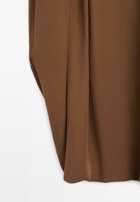 Brązowa tkanina o miękkiej fakturze, ozdobiona fałdami, wisząca delikatnie na białym tle.