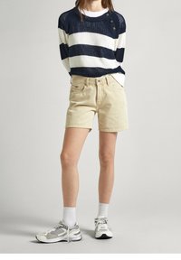 Suéter de rayas azul marino y blanco con grandes botones, combinado con pantalones cortos beige y zapatillas grises, acentuado con calcetines blancos hasta la altura del tobillo.