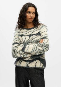 Sweter dziany o kremowej bazie z czarnymi i szarymi abstrakcyjnymi paskami, okrągłym dekoltem i luźnym krojem. Teksturowany, miękki materiał.