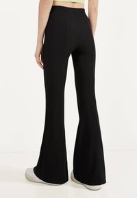 Svarta ribbade utsvängda byxor med hög midja, med en synlig söm längs sidorna och en slät textur, matchade med vita sneakers.