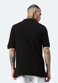 Polo shirt nero a maniche corte con colletto classico e vestibilità comoda. Presenta maniche arrotolate e dettagli di cucitura discreti.
