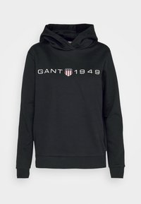 Sweat à capuche noir manches longues, avec le texte "GANT 1949" et un petit logo bouclier avec des étoiles et des rayures centré sur la poitrine.