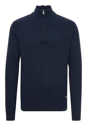 Tummansininen vetoketjullinen neulepaita, jossa on korkea kaulus ja puolipitkä vetoketju. Neulostekstuuri ja ribbireunat hihoissa sekä helmassa. Pieni logotäge alaosassa.