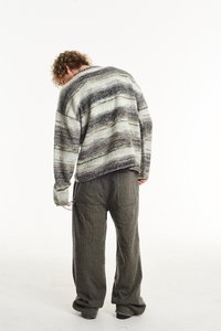 Didelis megztinis pilkų ir kreminių dryžių, pagamintas iš tekstūruoto megztinio audinio. Pasirinkta kartu su laisvai krentančiomis tamsiai pilkomis kelnėmis su kišenėmis.