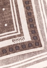 Hnědopískový šátek se vzorem, který obsahuje pruhy a čtvercové akcenty. Materiál má texturovaný vzhled. Logo "BOGGI MILANO" je viditelné.