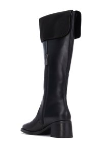 Botas de cuero negro hasta la rodilla con un puño de tela negra doblado, que cuentan con un cierre lateral y un tacón grueso con relieve.