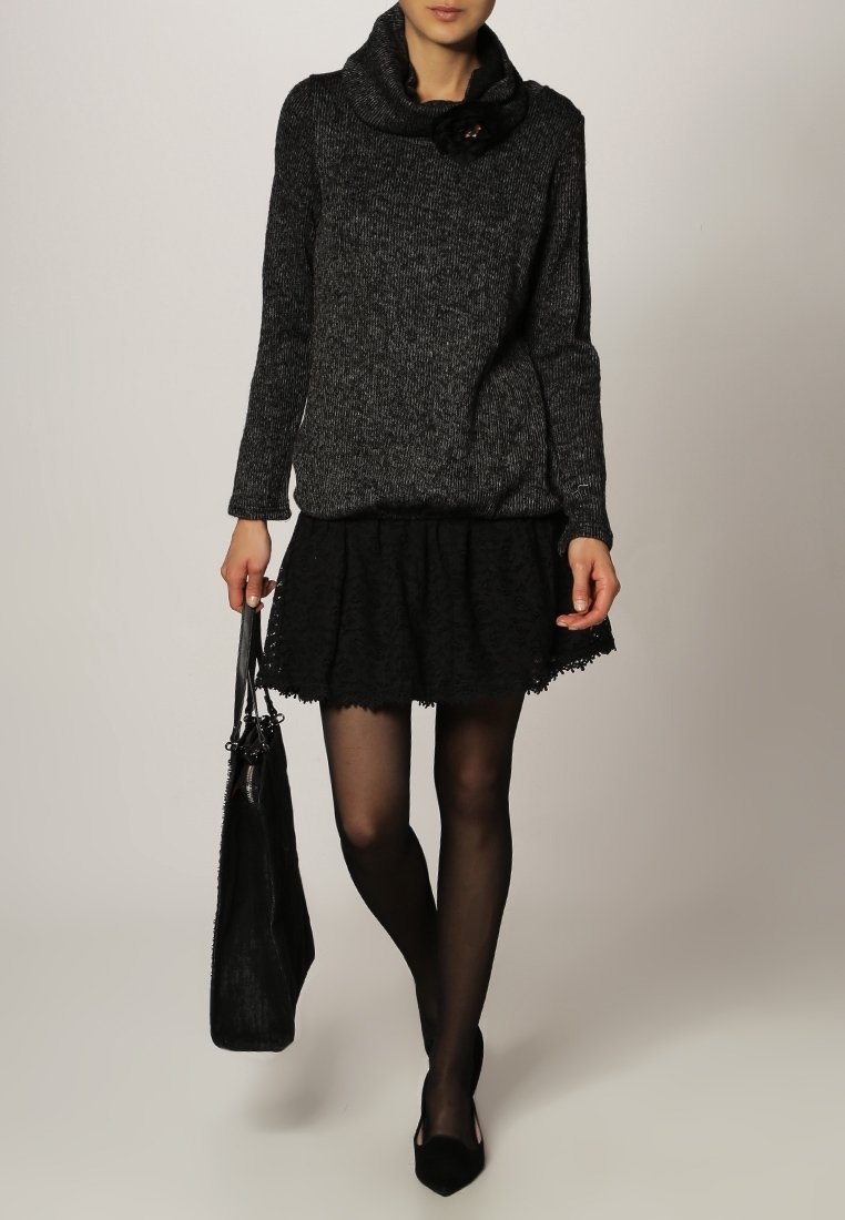 Lös svart och grå stickad tröja med en stor cowl-hals, ihop med en texturerad svart kjol och en svart handväska. Svarta strumpbyxor och klackar.