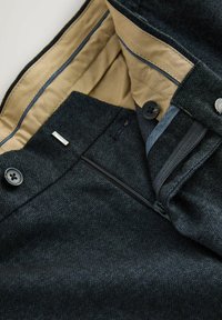 Dark gray textured trousers with a beige inner lining, unzipped fly, black buttons, and a small silver metal clasp near the waistband.