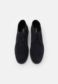 Bottines en daim bleu marine avec un design classique à lacets, bout arrondi, tige texturée et semelle plate en caoutchouc. Marque visible sur la semelle intérieure.