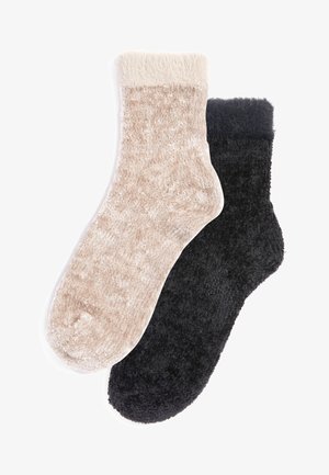 Dos pares de calcetines de felpa: uno beige con una textura suave y aterciopelada y un puño crema, y otro negro sólido con una suavidad similar.