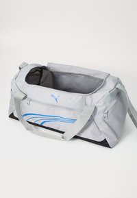 Grijze sporttas met blauw golvende patroon, gemaakt van duurzaam stof. Voorzien van twee draagriemen en een ritsvak aan één kant.