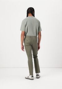 Chemise verte à manches courtes et pantalon olive tapered, en tissu doux. Des baskets blanches et noires complètent la tenue.