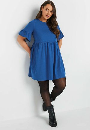 Robe bleue à manches courtes avec taille froncée, texture douce, manches évasées, accompagnée de collants noirs et de bottines noires chunky.