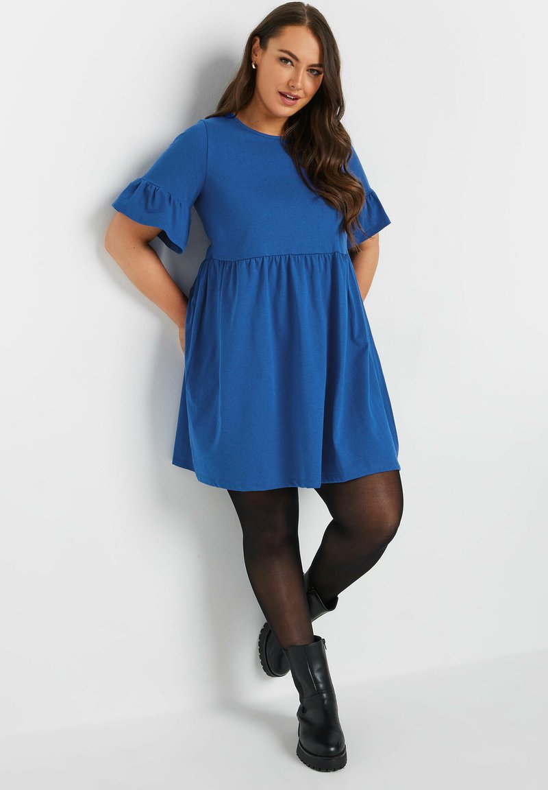 Blå kortärmad klänning med rynkad midja, mjuk textur, utsvängda ärmar, i kombination med svarta strumpbyxor och kraftiga svarta ankelboots.