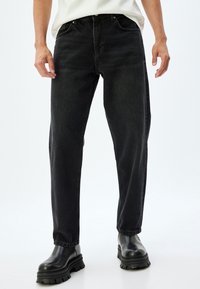 Jeans de mezclilla negra con corte recto, diseño de cinco bolsillos, sutil desgaste y detalles de costura. Combinados con botas negras gruesas.