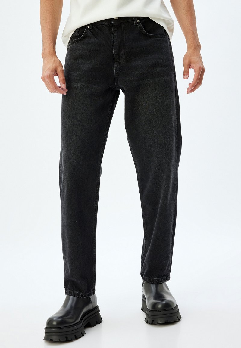 Jeans de mezclilla negra con corte recto, diseño de cinco bolsillos, sutil desgaste y detalles de costura. Combinados con botas negras gruesas.
