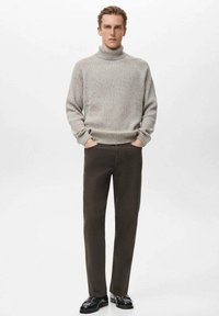 Suéter de cuello alto acanalado color gris claro, combinado con pantalones marrón oscuro. El conjunto presenta un ajuste relajado y se lleva con zapatos negros.