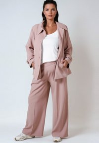 Light pink matching set featuring a button-up jacket with a collar and wide-leg pants, made of smooth fabric and paired with white sneakers.
