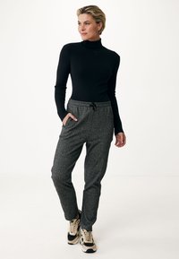 Černý rolák s ribovanou texturou, doplněný šedými vzorovanými tepláky s elastickým pasem a bočními kapsami, nošený s teniskami.