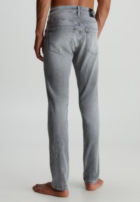 Šedé džíny z denimu se střihovým designem straight leg, s dvěma zadními kapsami a černou páskovou nášivkou. Tkanina má vybledlý vzhled.