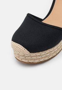 Espadrille compensée en toile noire avec semelle plateforme en jute tressée et détail de couture beige sur le bout.