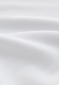 Měkká bílá tkanina s jemným diagonálním žebrováním a jemnými záhyby vytvářejícími hladký, plynulý povrch.