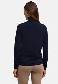 Marinefarbiger Rollkragenspullover aus einem glatten Strickstoff, mit langen Ärmeln und einem abgerundeten Saum, kombiniert mit beigen, figurbetonten Hosen.