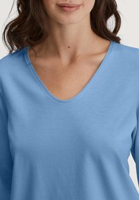 Lichtblauw langarmshirt met een V-halsontwerp, gemaakt van een gladde stof, met een ontspannen pasvorm en minimale stikseldetails.