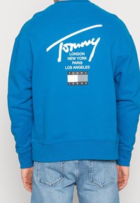 Blauer Sweatshirt mit weißem Logo und Städtenamen auf dem Rücken. Gerippte Bündchen und Saum, lockere Passform, aus weichem Baumwollmischgewebe hergestellt.