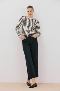 Gestreiftes Langarmshirt in Schwarz und Weiß, kombiniert mit hoch taillierten dunklen Hosen und schwarzen Blockabsatzschuhen. Schlichter Gürtel-Akzent.